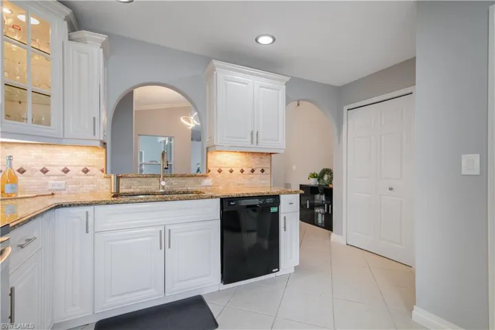 Kitchen with black dishwasher, light granite countertops, sink, white cabinets.