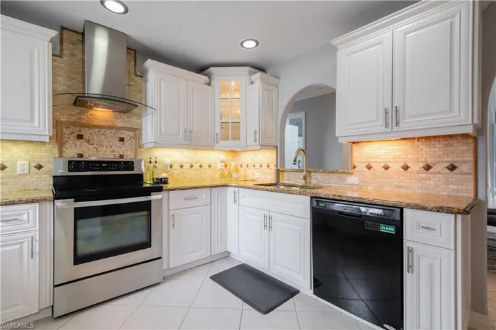 Kitchen with wall chimney range hood, white cabinetry, black dishwasher, and electric range