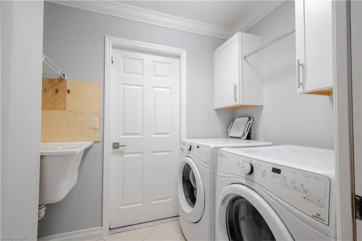 Washroom featuring cabinets, crown molding, washer and clothes dryer, and light tile patterned floors