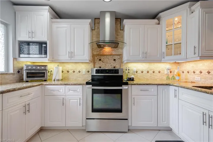Kitchen featuring tasteful backsplash, wall chimney range hood, stainless steel appliances, white cabinets, and light stone counters