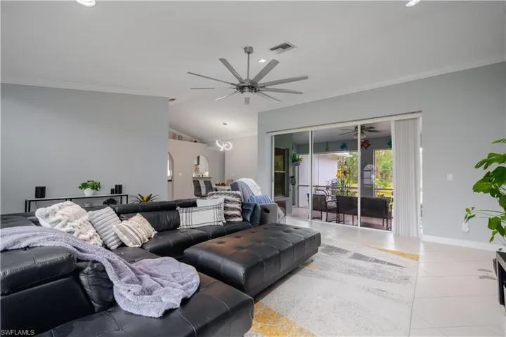 Living room with vaulted ceiling, crown molding, light tile patterned floors, and ceiling fan