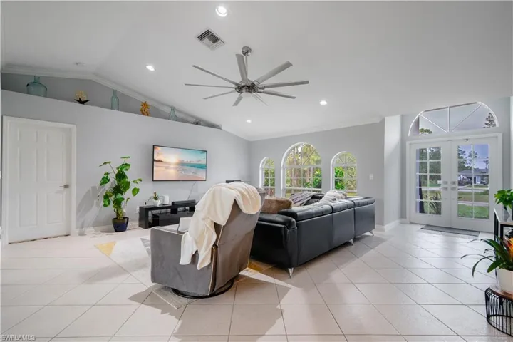 Tiled living room featuring french doors, ceiling fan, crown molding, and lofted ceiling