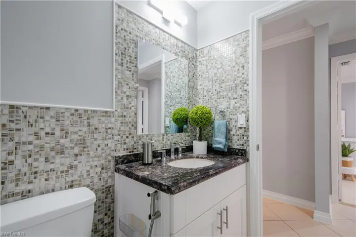 Bathroom featuring tile patterned floors, toilet, crown molding, vanity, and tasteful backsplash