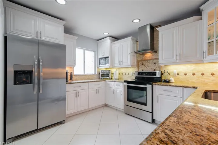 Kitchen featuring white cabinets, backsplash, light stone countertops, wall chimney exhaust hood, and stainless steel appliances