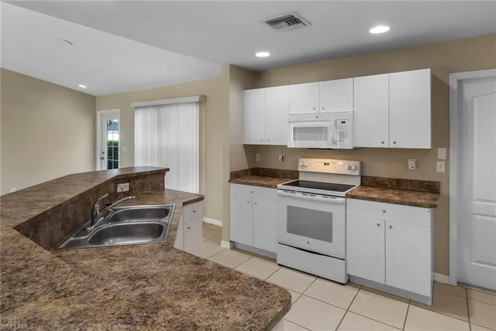 Kitchen featuring white appliances, dark countertops, white cabinetry, light tile patterned floors, and recessed lighting