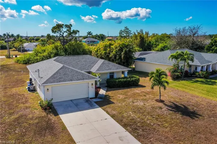 Ranch-style home with a shingled roof, concrete driveway, a front lawn, and stucco siding