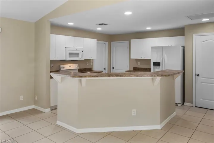 Kitchen with a breakfast bar area, white appliances, white cabinetry, recessed lighting, and light tile patterned floors