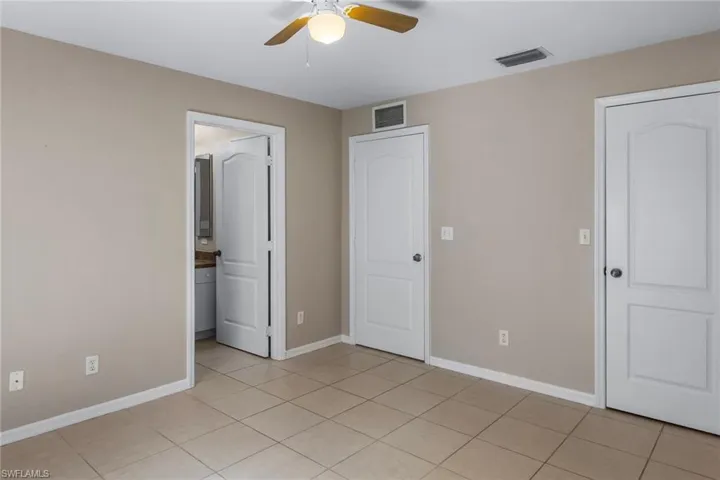 Unfurnished bedroom featuring a ceiling fan, ensuite bathroom, and light tile patterned flooring