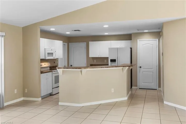 Kitchen featuring a breakfast bar, white appliances, dark countertops, white cabinetry, and recessed lighting
