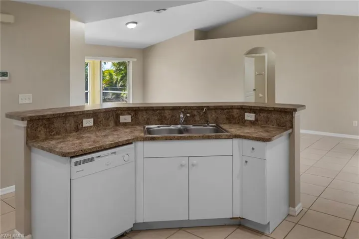 Kitchen with white cabinetry, dark countertops, light tile patterned flooring, white dishwasher, and arched walkways