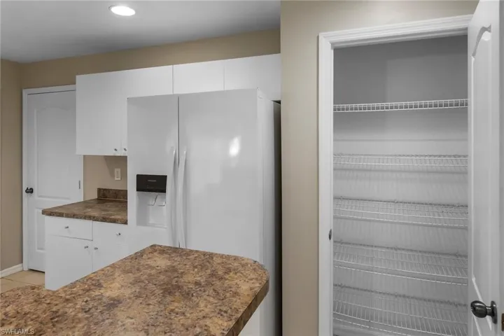 Kitchen with white refrigerator with ice dispenser, white cabinets, dark countertops, and recessed lighting