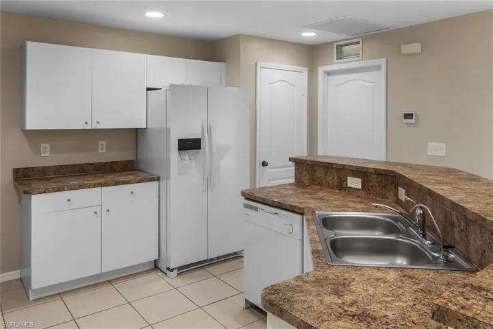 Kitchen with dark countertops, white appliances, light tile patterned flooring, white cabinets, and recessed lighting