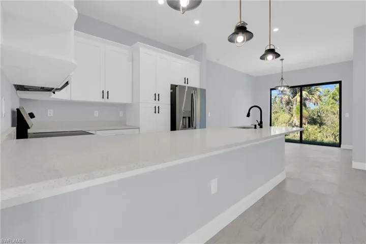 Kitchen featuring a peninsula, light stone counters, stainless steel fridge with ice dispenser, stove, and pendant lighting
