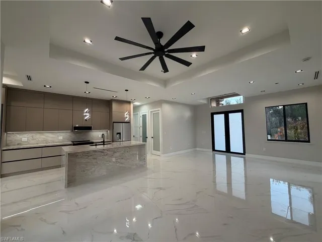 Unfurnished living room featuring a tray ceiling, a ceiling fan, light marble finish floors, and recessed lighting
