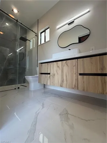 Bathroom featuring vanity, a marble finish shower, and light marble finish flooring