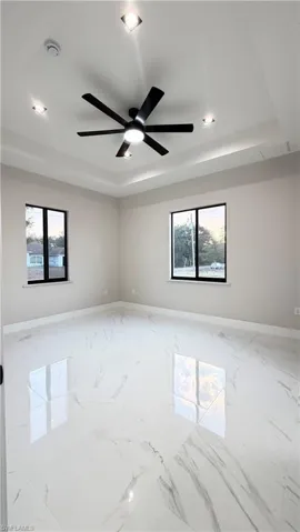 Unfurnished room with a tray ceiling, ceiling fan, and marble finish flooring