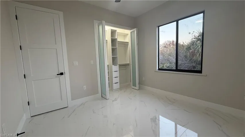 Unfurnished bedroom with a walk in closet and light marble finish flooring