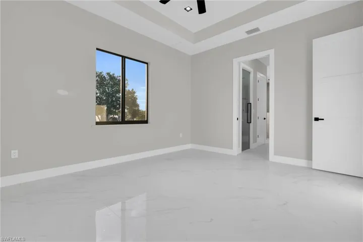 Empty room featuring light marble finish flooring, ceiling fan, and a tray ceiling