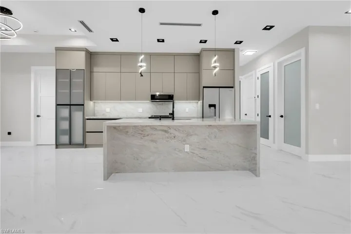 Kitchen featuring modern cabinets, gray cabinets, hanging light fixtures, stainless steel appliances, and a kitchen island with sink