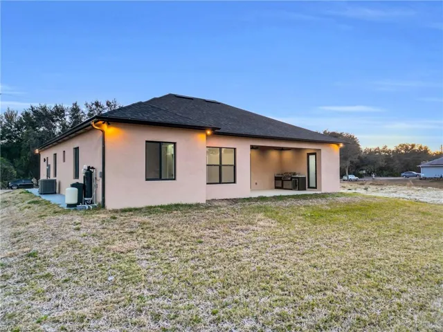 Back of property at dusk with a patio area, stucco siding, a yard, and roof with shingles