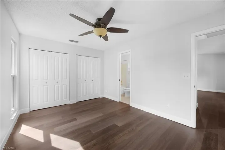 Unfurnished bedroom featuring multiple closets, a textured ceiling, dark wood-style flooring, a ceiling fan, and connected bathroom