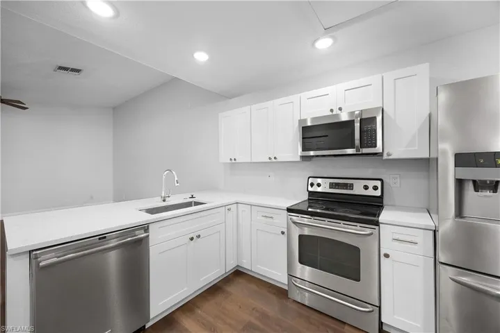 Kitchen featuring appliances with stainless steel finishes, dark wood-style floors, white cabinets, a peninsula, and recessed lighting