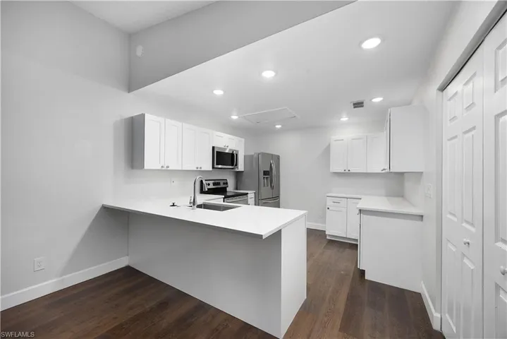 Kitchen with a peninsula, white cabinetry, dark wood-style flooring, and recessed lighting