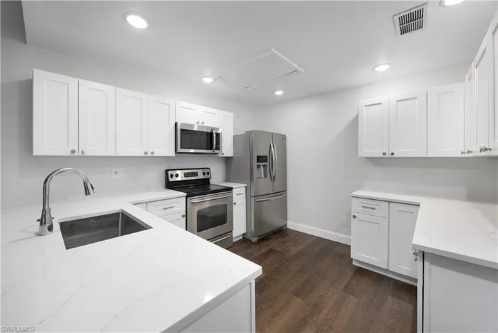 Kitchen featuring appliances with stainless steel finishes, white cabinetry, light stone counters, dark wood-type flooring, and recessed lighting
