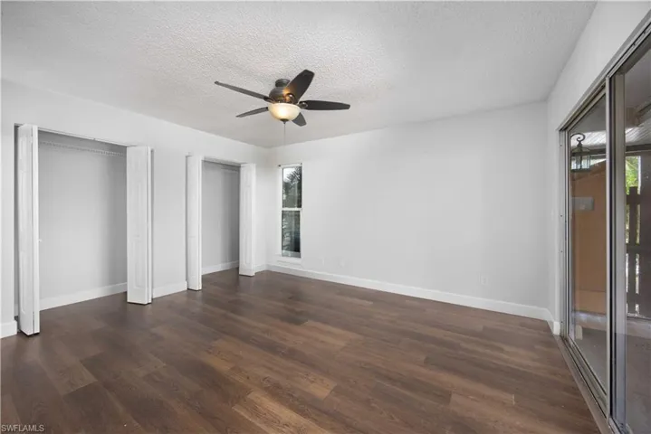 Unfurnished bedroom featuring multiple closets, a textured ceiling, dark wood-type flooring, ceiling fan, and access to exterior