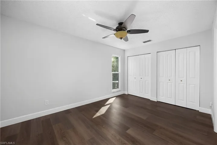 Unfurnished bedroom with two closets, a textured ceiling, dark wood-style floors, and a ceiling fan