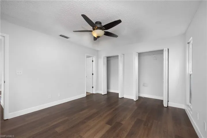 Unfurnished bedroom with two closets, a textured ceiling, dark wood-style floors, and ceiling fan