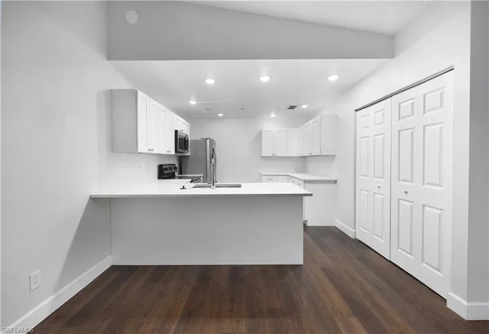 Kitchen with white cabinetry, dark wood-style floors, stainless steel appliances, recessed lighting, and a peninsula
