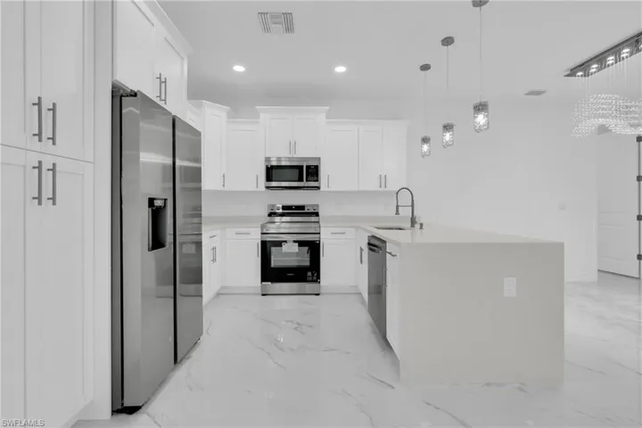 Kitchen with a peninsula, appliances with stainless steel finishes, white cabinets, light stone counters, and recessed lighting