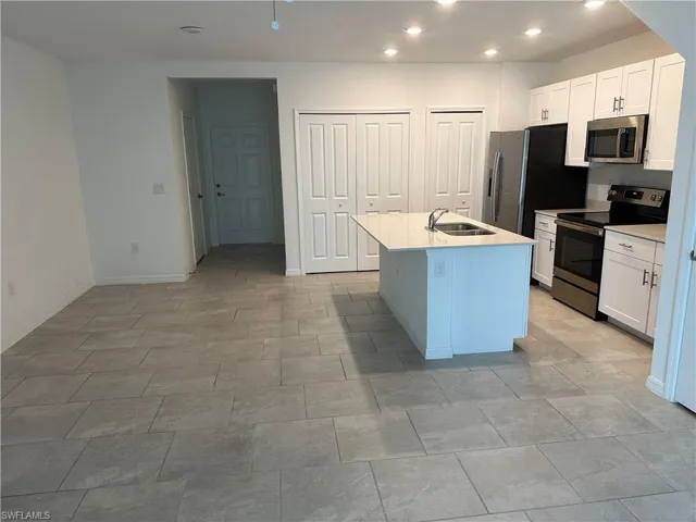 Kitchen with a center island with sink, appliances with stainless steel finishes, white cabinetry, and light tile floors