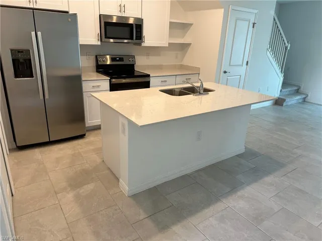 Kitchen with appliances with stainless steel finishes, white cabinets, light tile floors, and a center island with sink