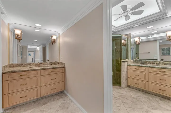 Bathroom featuring ornamental molding, two vanities, a shower stall, recessed lighting, and a ceiling fan