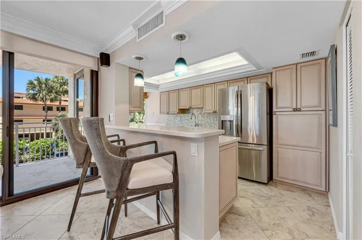 Kitchen with stainless steel fridge with ice dispenser, light countertops, pendant lighting, light brown cabinetry, and crown molding