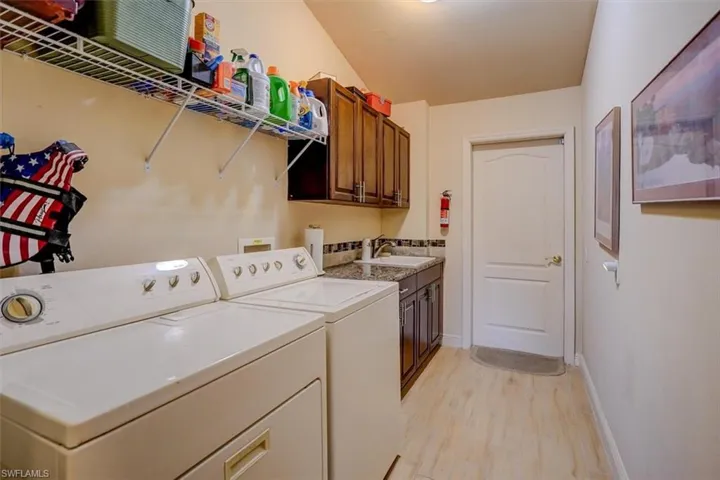 Laundry area with washing machine and clothes dryer, light hardwood / wood-style floors, cabinets, and sink