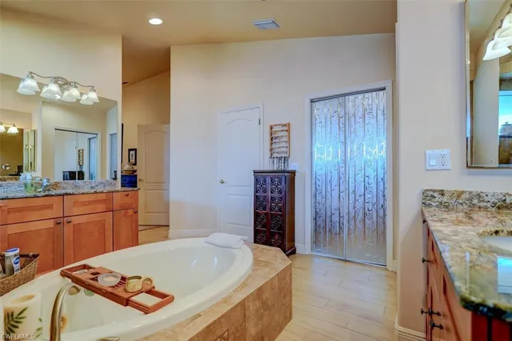 Bathroom featuring lofted ceiling, tiled tub, hardwood / wood-style flooring, and vanity