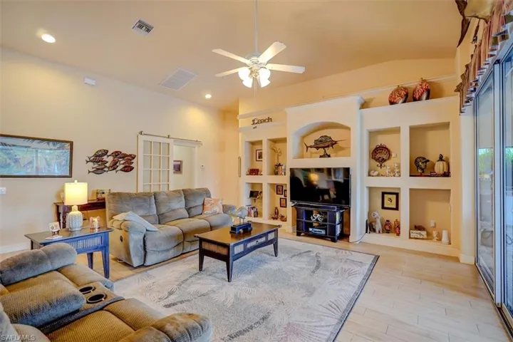 Living room featuring built in shelves, light wood-type flooring, vaulted ceiling, and ceiling fan
