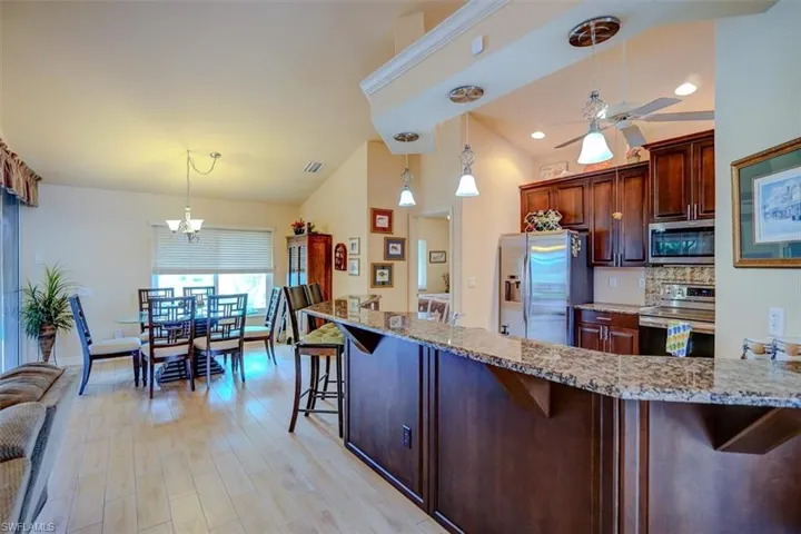 Kitchen with light hardwood / wood-style flooring, appliances with stainless steel finishes, hanging light fixtures, and a breakfast bar area