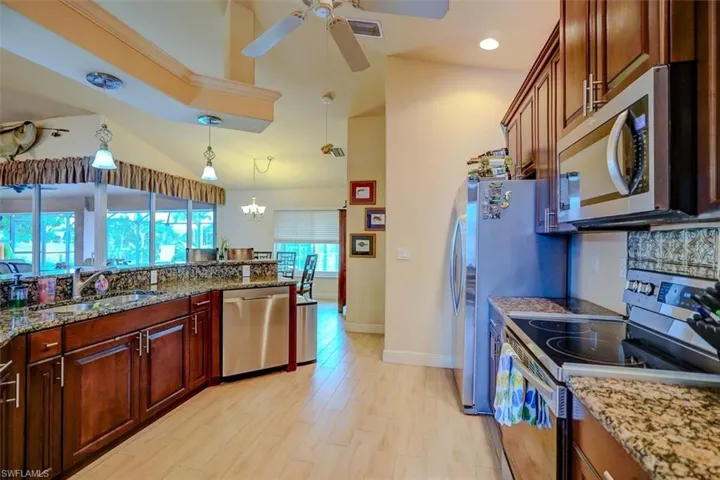 Kitchen with light wood-type flooring, hanging light fixtures, sink, appliances with stainless steel finishes, and light stone countertops