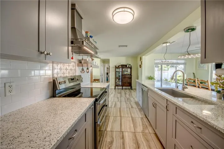 Kitchen with appliances with stainless steel finishes, tasteful backsplash, light stone countertops, wall chimney range hood, and gray cabinets