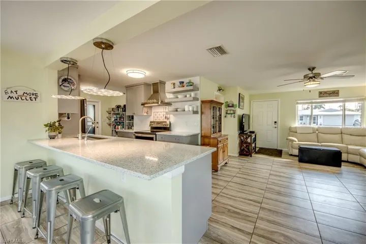 Kitchen featuring pendant lighting, open shelves, light stone countertops, a kitchen bar, and stainless steel appliances