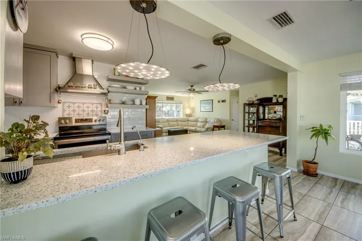 Kitchen with light stone counters, stainless steel range with electric stovetop, wall chimney exhaust hood, and a kitchen breakfast bar