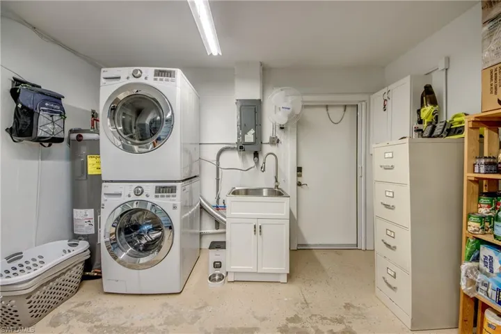 Laundry room with electric panel, electric water heater, stacked washer / drying machine, cabinet space, and concrete flooring