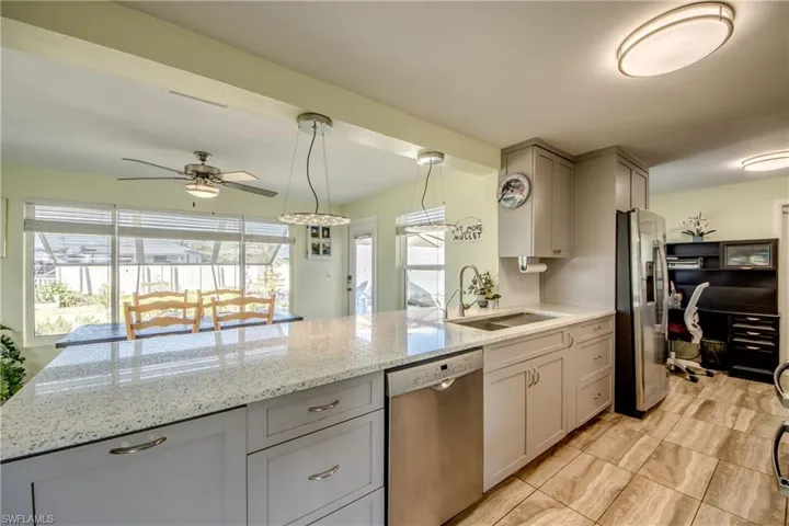Kitchen with light stone counters, appliances with stainless steel finishes, decorative light fixtures, gray cabinets, and a ceiling fan