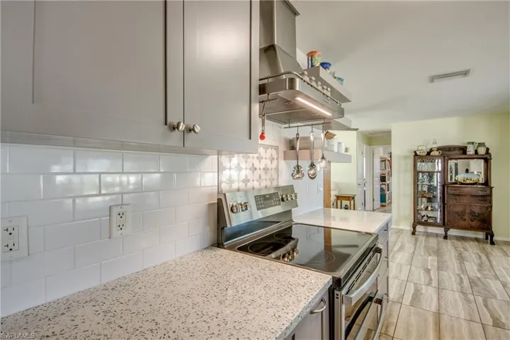 Kitchen featuring stainless steel electric range, decorative backsplash, range hood, and light stone counters