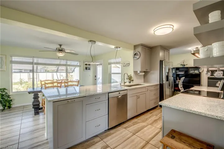 Kitchen with gray cabinetry, light stone counters, decorative light fixtures, stainless steel appliances, and a peninsula