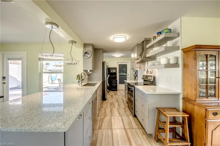 Kitchen with appliances with stainless steel finishes, light stone countertops, open shelves, and gray cabinetry